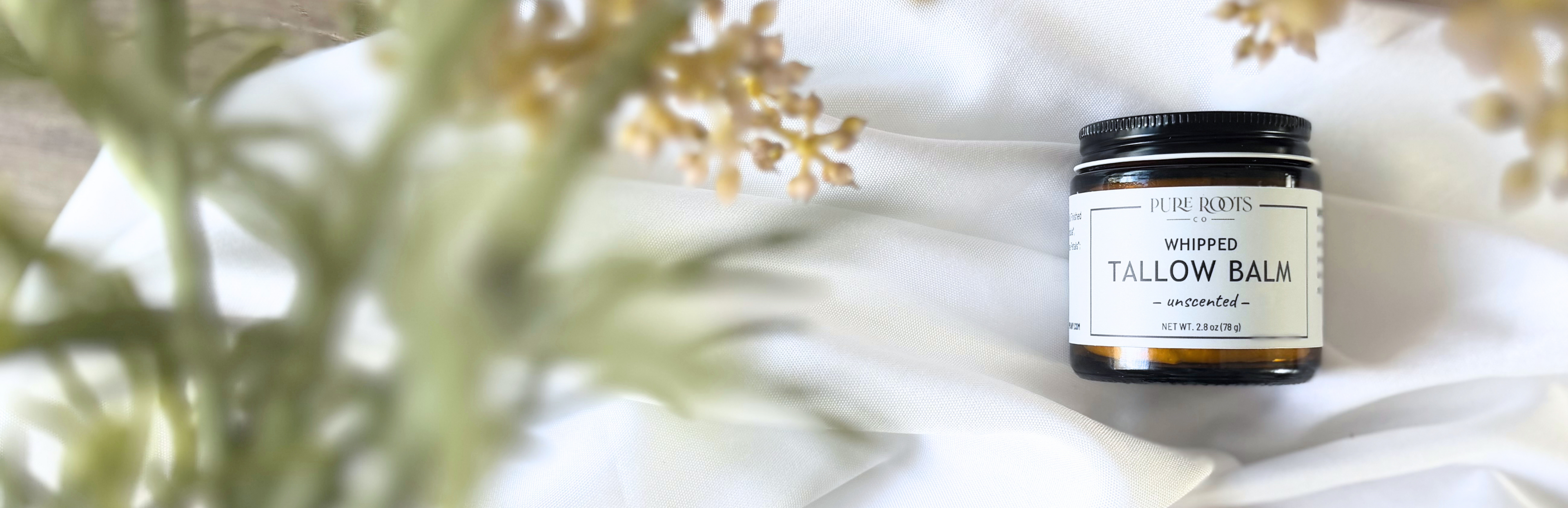 Jar of whipped tallow balm with a white background and blurred greenery
