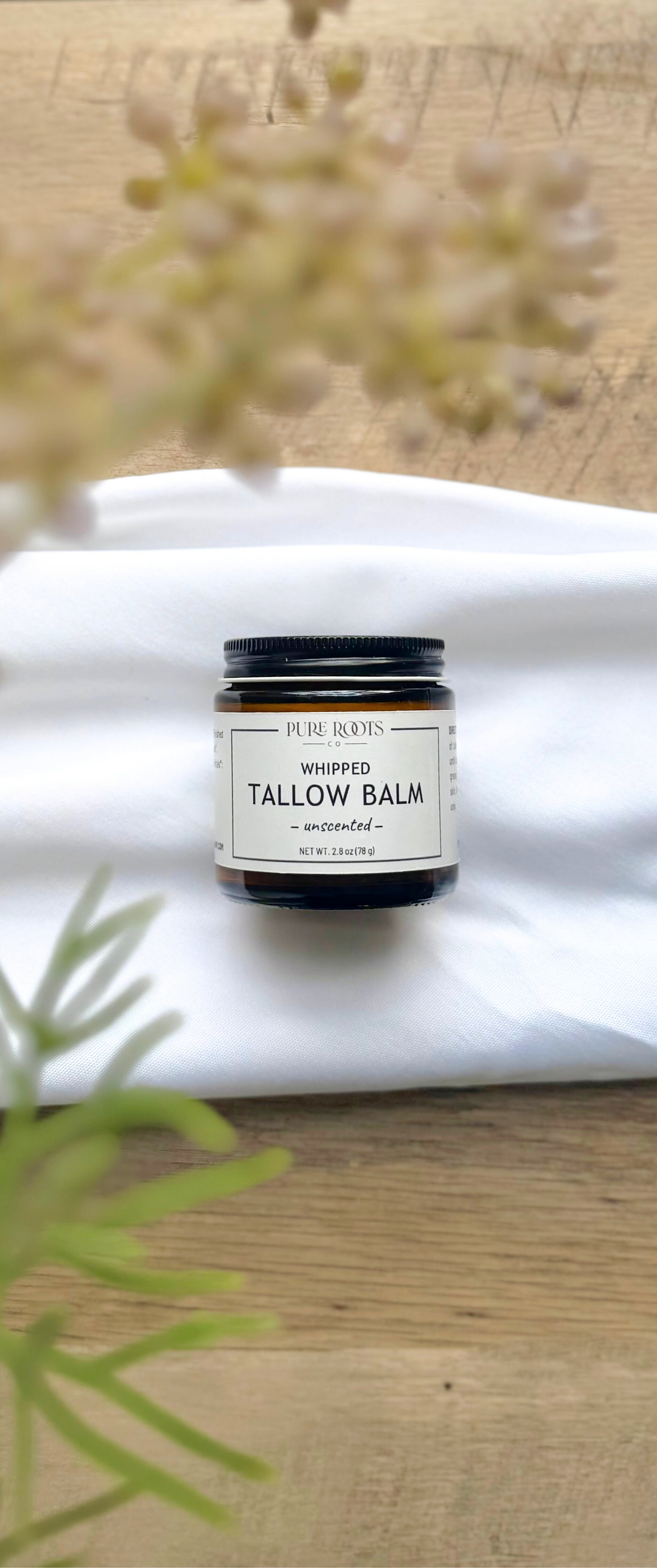 Jar of whipped tallow balm on a white cloth with natural elements in the background